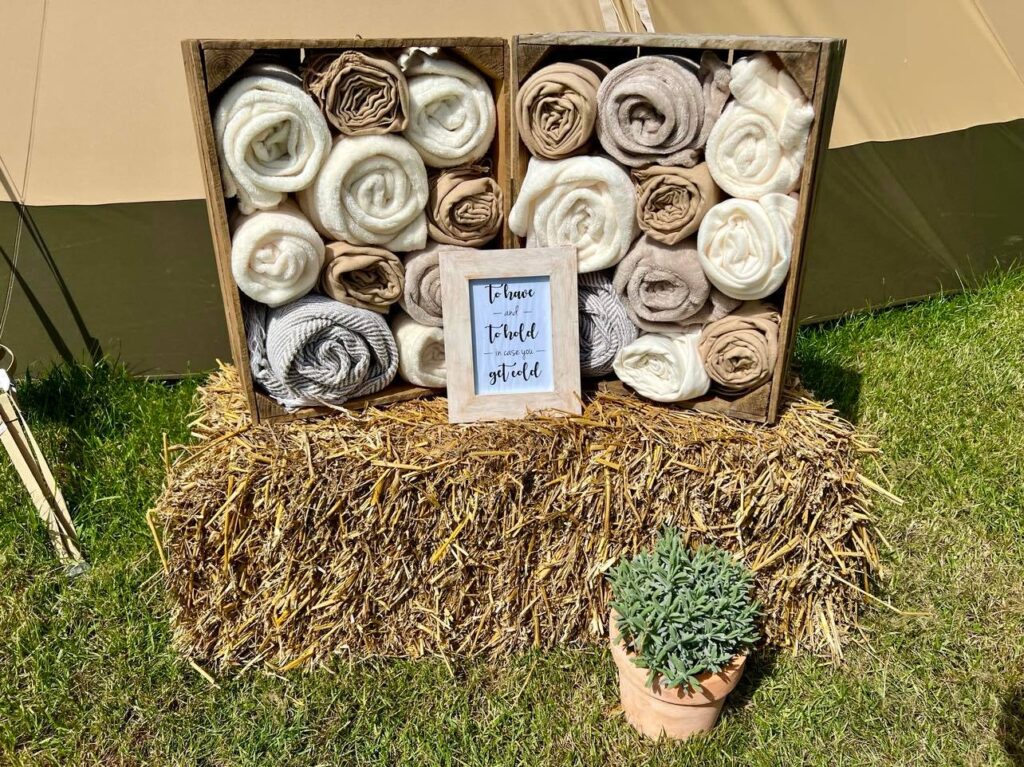 Two crates of neutral coloured blankets sat on a straw bale with a sign that reads To have and to hold in case you get cold | Blanket Hire Lincolnshire