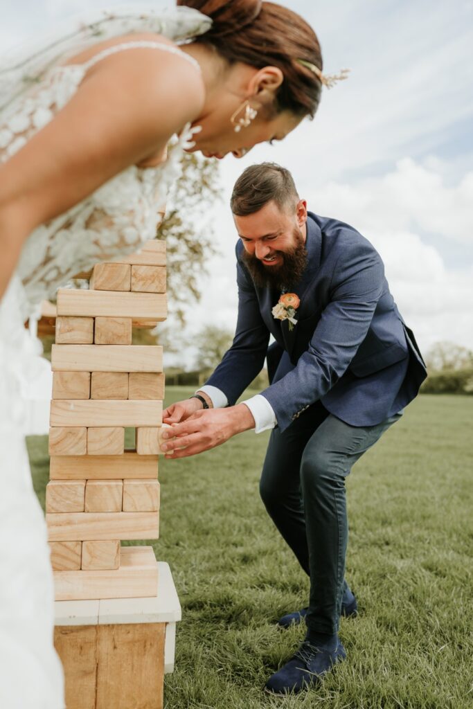 A bride and groom playing a game of giant Jenga on their wedding day. Lots of smiles and happy faces as this luxury garden game keeps them entertained | Giant Jenga Garden Game Hire UK