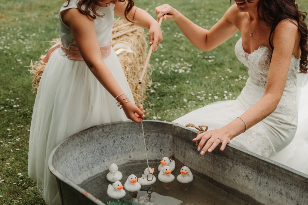 A child and bride playing hook a duck at a wedding. A luxury version of the game in a vintage metal bath with white ducks.