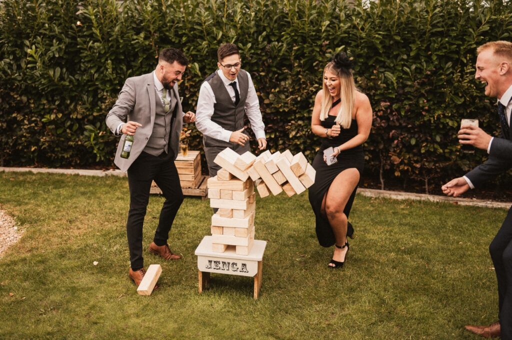 People playing giant jenga at a wedding at Inkersall Grange Farm Nottinghamshire. The Jenga is toppling down as the guests are laughing and smiling. Luxury garden games hire from Emma Lane Designs