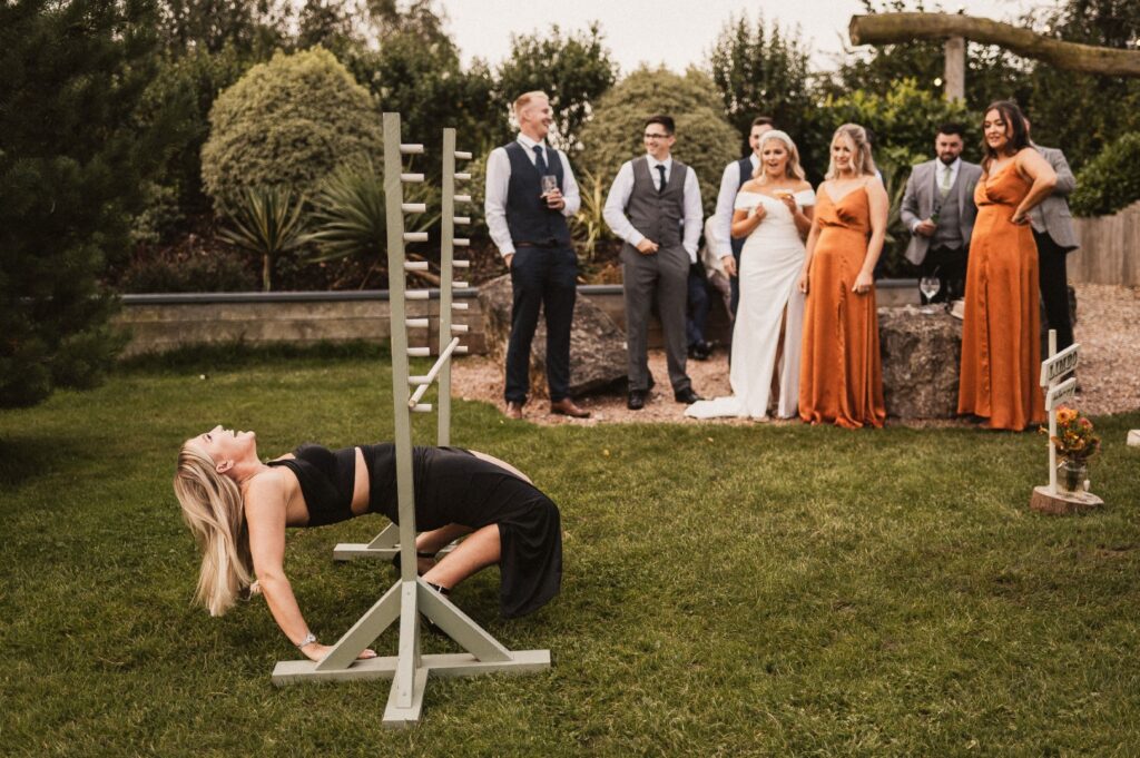 Wedding guests are stood watching as a woman plays Limbo and is falling backwards.