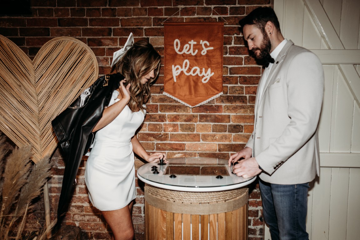 A bride and groom playing a retro arcade game available to hire from Emma Lane Designs as part of their indoor games hire collection